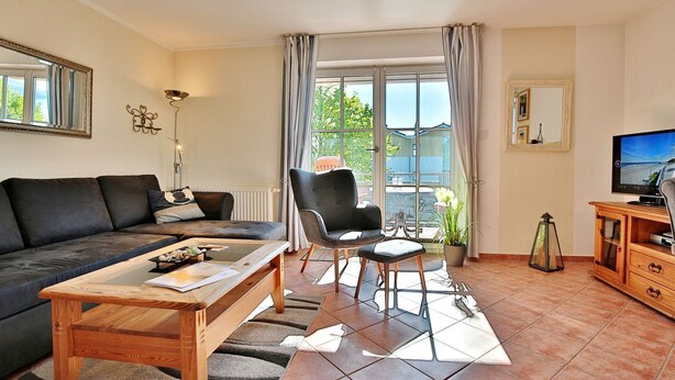 A living room with a sofa, a chair, a coffee table, a TV, and a balcony with curtains.