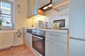 Una cocina con armarios blancos, estufa, horno y microondas. Hay una ventana con una planta y un adorno de pájaro.