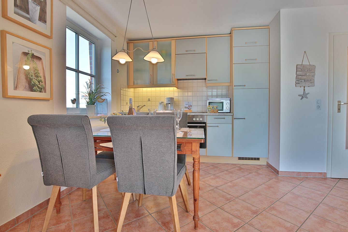 Un coin repas avec deux chaises grises, une table en bois et, au fond, une cuisine avec des meubles bleu clair et un four à micro-ondes.