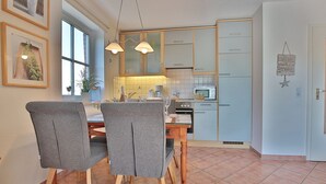A dining area with two grey chairs, a wooden table, and a kitchen in the background with light blue cabinets and a microwave.