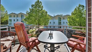 A balcony with a round table and two wooden chairs, overlooking a row of buildings and trees.