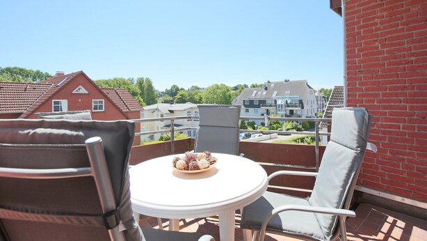 A balcony with a round table and two chairs, a bowl of snacks, and a view of neighboring houses.