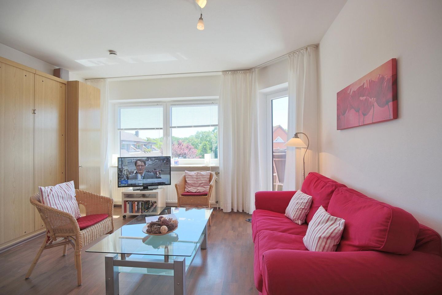 A living room with a red sofa, wicker chairs, a glass coffee table, and a TV on a stand.