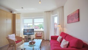 A living room with a red sofa, wicker chairs, a glass coffee table, and a TV on a stand.