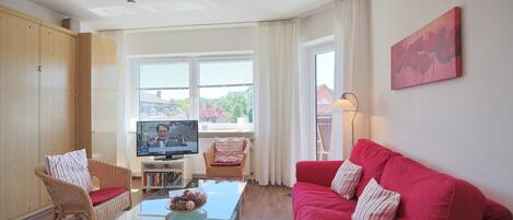 A living room with a red sofa, wicker chairs, a glass coffee table, and a TV on a stand.
