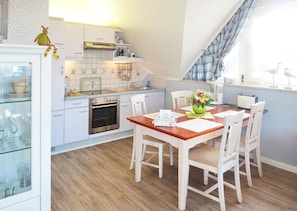 Une cuisine moderne avec des armoires blanches, un four encastré et un coin repas comprenant une table et des chaises en bois.