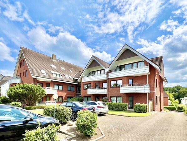 A modern apartment building with multiple balconies, a parking area, and well-maintained landscaping.