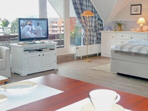 A modern living room with a television, white furniture, a dining table with white plates, and a view of the outside.