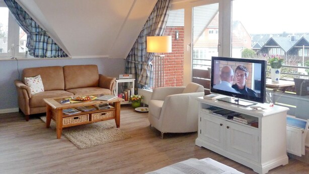 A cozy living room with a brown sofa, a white armchair, a coffee table, and a TV on a white cabinet.