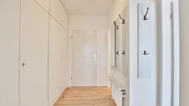 Un couloir étroit aux murs blancs, doté d’un plancher en bois et d’un radiateur blanc.