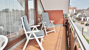 A balcony with two striped lounge chairs, a brick wall, and a view of a street with buildings and cars.