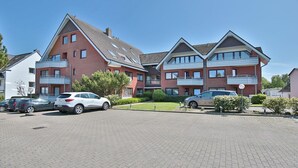 A multi-story residential building with a brick facade, multiple balconies, and a parking area with several cars.