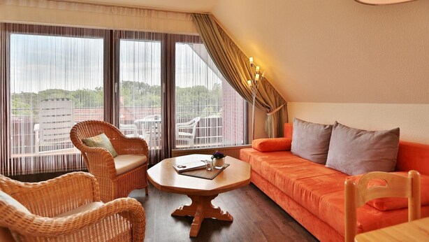 A room with a sofa, two wicker chairs, a table, and a balcony with a view.