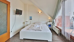 A modern hotel room with a large bed, a TV, a small table, a lamp, and a view of the outside.