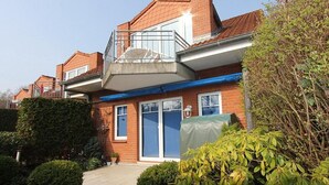 A two-story residential building with a balcony, brick exterior, and a covered front porch. - Terraced house Eichenweg - Terraced house Eichenweg Apartment 8 (Scharbeutz)