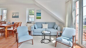 A modern living room with a blue sofa, two armchairs, a coffee table, and a dining area with a wooden table and chairs. - Terraced house Eichenweg - Terraced house Eichenweg Apartment 8 (Scharbeutz)
