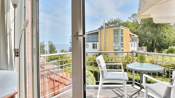 A balcony with a glass door, white chairs, a small table, and a view of a yellow building with a balcony. - Terraced house Eichenweg - Terraced house Eichenweg Apartment 8 (Scharbeutz)