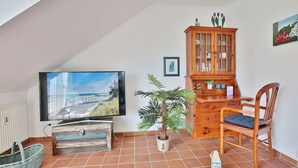 A living room with a television, wooden cabinet, chair, potted plant, and tiled floor. - Terraced house Eichenweg - Terraced house Eichenweg Apartment 8 (Scharbeutz)