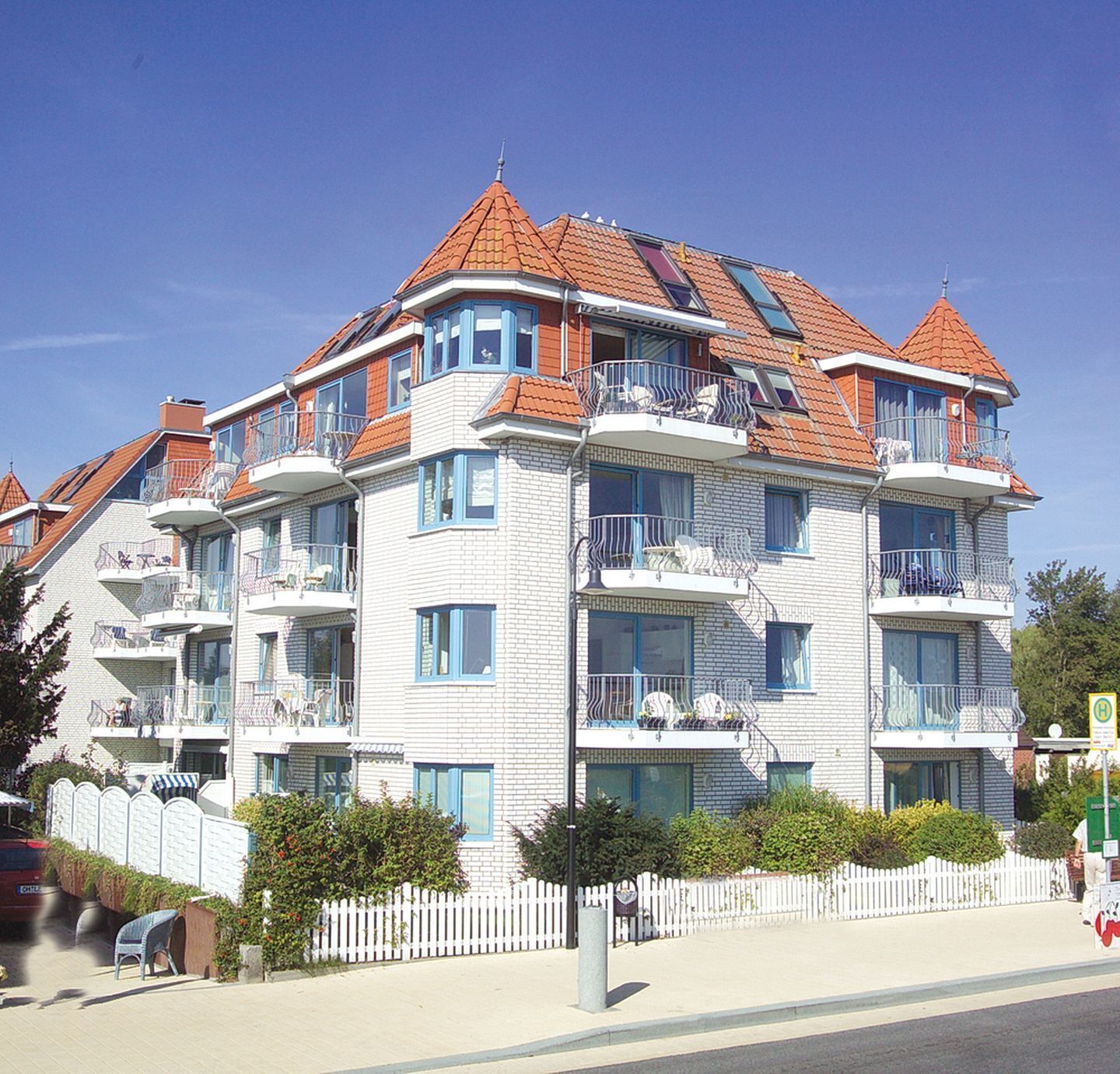 A multi-story building with balconies, a white facade, and red-tiled roofs.