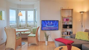 Un salon moderne comprenant un coin repas, un téléviseur fixé au mur et une bibliothèque.