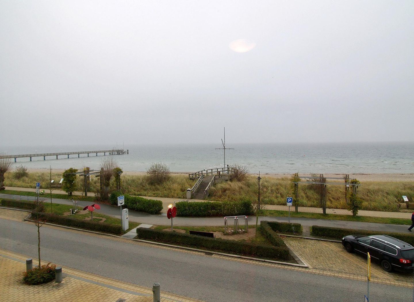 A coastal road with a pedestrian path, a bridge in the distance, and a beach.