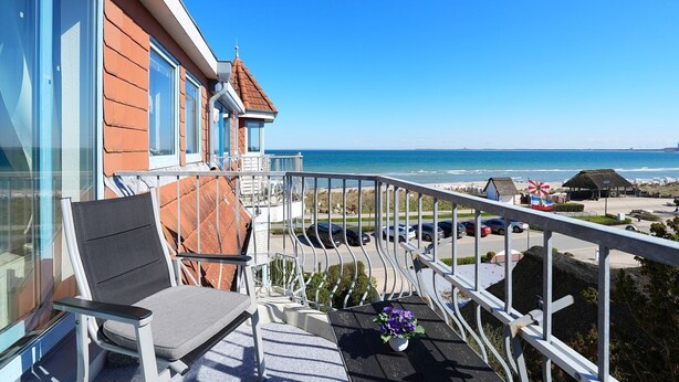 A balcony with a chair, a small table with a flower, and a view of the beach and ocean. - Strandschlösschen Appartement 15 - Strandschlößchen (Scharbeutz)