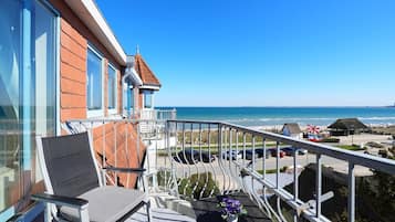 Ein Balkon mit Stuhl, einem Tisch mit Blume und Blick auf Strand und Meer.