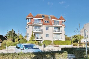 Un edificio residencial de varios pisos con techo de tejas rojas, balcones y cerca de piquetes blancos.