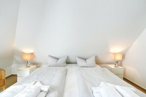 Ein Schlafzimmer mit zwei Betten, weißen Laken, zwei Nachttischlampen und Holzboden.