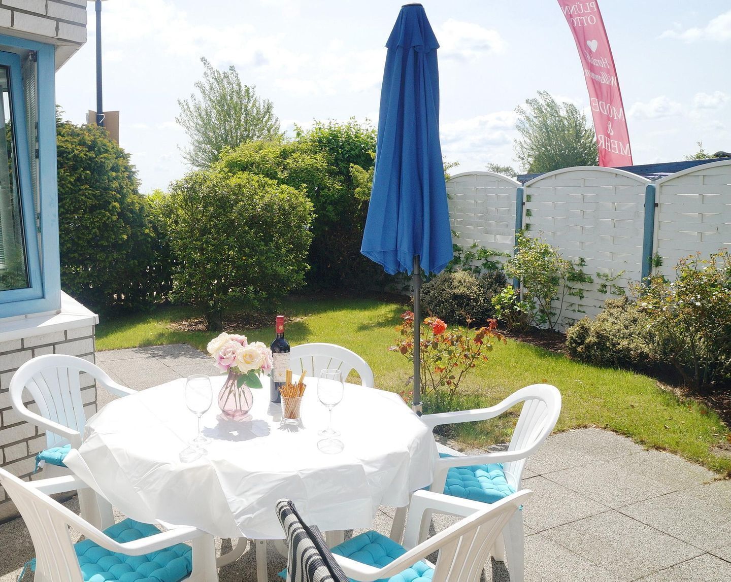 Un patio esterno con un tavolo rotondo, sedie bianche e un ombrellone blu.