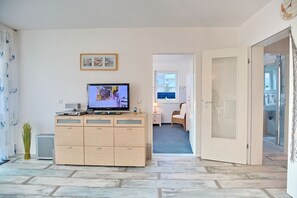 A modern living room with a flat-screen TV, a wooden cabinet, a small plant, and a view into the adjacent room. - Barke Apartment 1 - Barke (Scharbeutz)