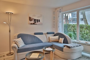 A modern living room with a curved sofa, a small round table, and a floor lamp. - Barke Apartment 1 - Barke (Scharbeutz)