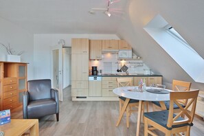 A modern kitchen with wooden cabinets, a dining table with chairs, and a lofted sleeping area with a skylight.