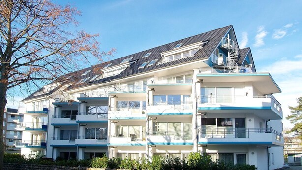 A multi-story residential building with balconies, a sloped roof, and a stone wall in front. - Barque Apartment 404 - Barque (Scharbeutz)