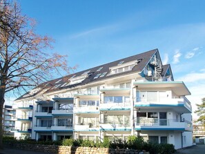 A multi-story residential building with balconies, a sloped roof, and a stone wall in front.