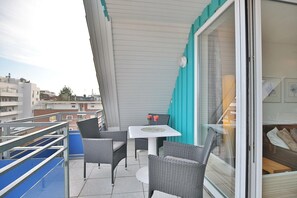 A balcony with wicker furniture, a table, and a window with curtains.