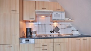 A modern kitchen with light wood cabinets, a built-in microwave, a coffee maker, and a stove. - Barque Apartment 404 - Barque (Scharbeutz)