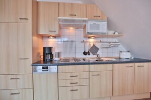 A modern kitchen with light wood cabinets, a built-in microwave, a coffee maker, and a stove. - Barque Apartment 404 - Barque (Scharbeutz)