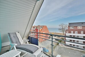 A balcony with a view of the sea, a red brick building, and a parking area. - Barque Apartment 404 - Barque (Scharbeutz)