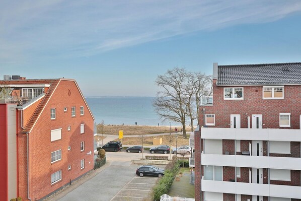A residential building with a view of the sea, featuring a parking area and a pathway leading to the beach.