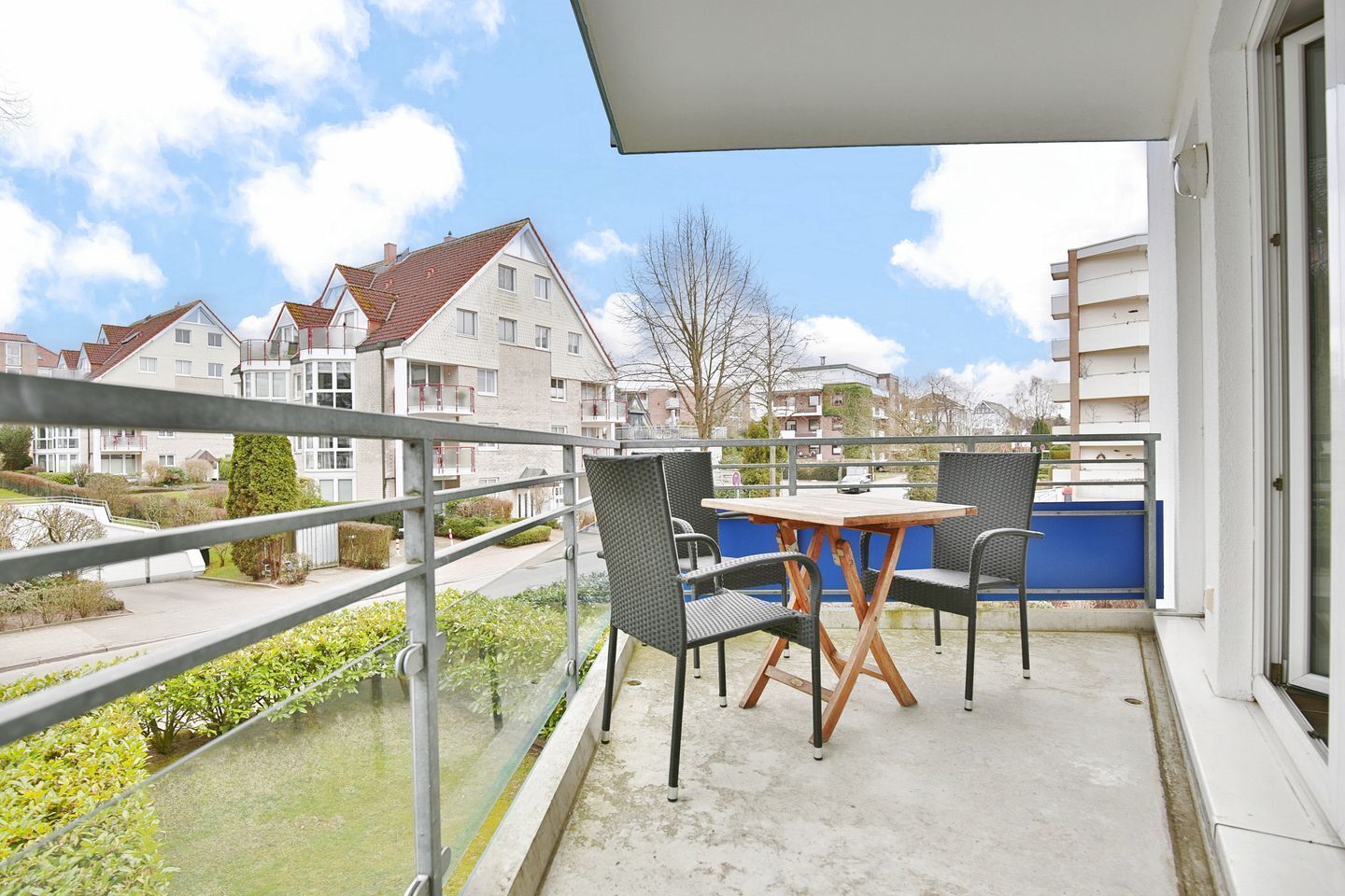 A balcony with a table and chairs, overlooking a residential area with houses and a clear sky.