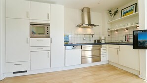 Una cocina moderna con armarios blancos, electrodomésticos de acero inoxidable y un televisor de pantalla plana montado en la pared.