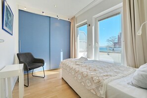 A bedroom with a bed, a chair, a desk, and a large window with a view. - Barke Apartment 324 - Barke (Scharbeutz)