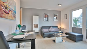 Ein modernes Wohnzimmer mit einer Couch, einem Couchtisch und einem Esstisch. An den Wänden hängen gerahmte Bilder und über der Couch hängt ein großes Gemälde.
