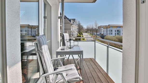 Ein Balkon mit Tisch und Stühlen, Blick auf Gebäude, und einer Brüstung.