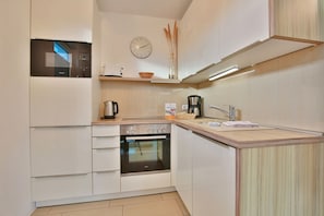 A compact kitchen with a microwave, stove, oven, and a sink. - Strandglück Apartment 14C - Strandglück Haus C (Scharbeutz)