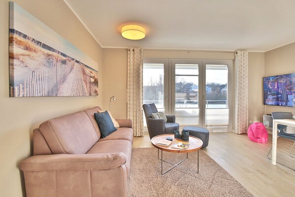 A modern living room with a sofa, armchair, coffee table, and a television. - Strandglück Apartment Strand 6 - Strandglück House C (Scharbeutz)