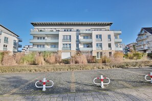 A multi-story residential building with balconies, a paved area with bollards, and a clear sky. - Strandglück Apartment Strand 6 - Strandglück House C (Scharbeutz)