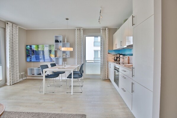 A modern apartment with a dining area, kitchen, and a large TV screen.