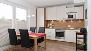 A modern kitchen with a dining area, featuring a wooden table, black chairs, a built-in oven, and a microwave. - Strandglück Apartment 15C - Strandglück House C (Scharbeutz)